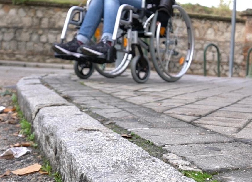 Persona en silla de ruedas, al borde de la vereda queriendo cruzar la calle